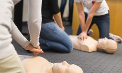 A group of adult education students practitcing CPR chest compressioon on a dummy.